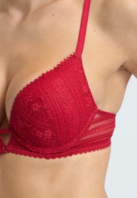 Roter Spitzen-BH mit zarten Blumenmustern, verstellbaren Trägern und gewelltem Rand entlang der Cups und des Bands, entworfen für Unterstützung.