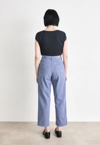 Jeans de cintura alta, azul claro, com um ajuste solto, apresentando dois bolsos traseiros e uma etiqueta da marca em tom de cáqui. Blusa preta de mangas curtas com tecido texturizado.
