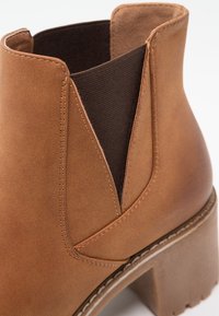 Bottine en cuir brun avec un panneau latéral élastique et un talon épais, exhibant des coutures détaillées et une texture lisse.