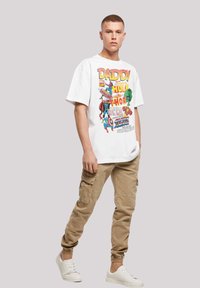 Hvit grafisk T-skjorte med superhelt-design, beige cargo-bukser og hvite sneakers. T-skjorten har fargerik tekst og figurer.