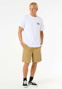 White short-sleeve t-shirt with orange and black "Ripcurl" logo, paired with tan corduroy shorts. Black sneakers with white soles and socks.