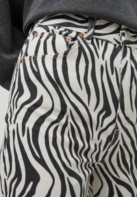 Jean en denim noir et blanc à rayures zébrées, avec une conception classique à cinq poches et des rivets en cuivre, présentant une légère texture et une coupe ajustée.