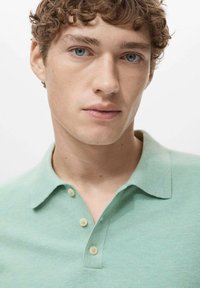Polo shirt verde chiaro in tessuto testurizzato, con colletto, tre bottoni e vestibilità classica. Il colore è morbido, con leggere variazioni.