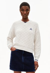 Witte textuur gebreide trui met een V-hals en marineblauwe accenten, gecombineerd met een donkergrode corduroy rok. Voorzien van geribde mouwen en zoom.