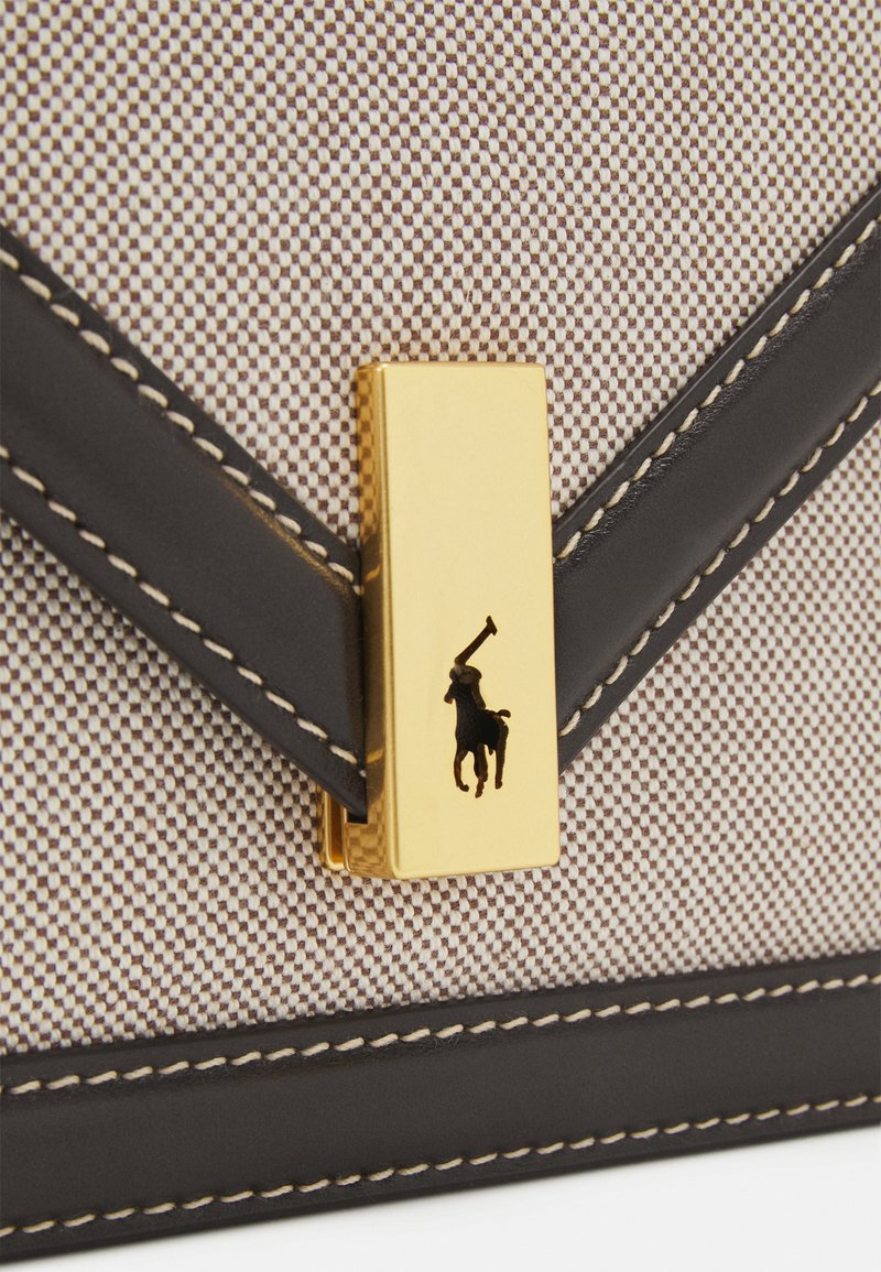 Brązowa i biała torebka z teksturowanej tkaniny z pozłacanym metalowym zapięciem, które zawiera logo oraz ciemne skórzane akcenty, ukazująca staranne detale przeszycia.