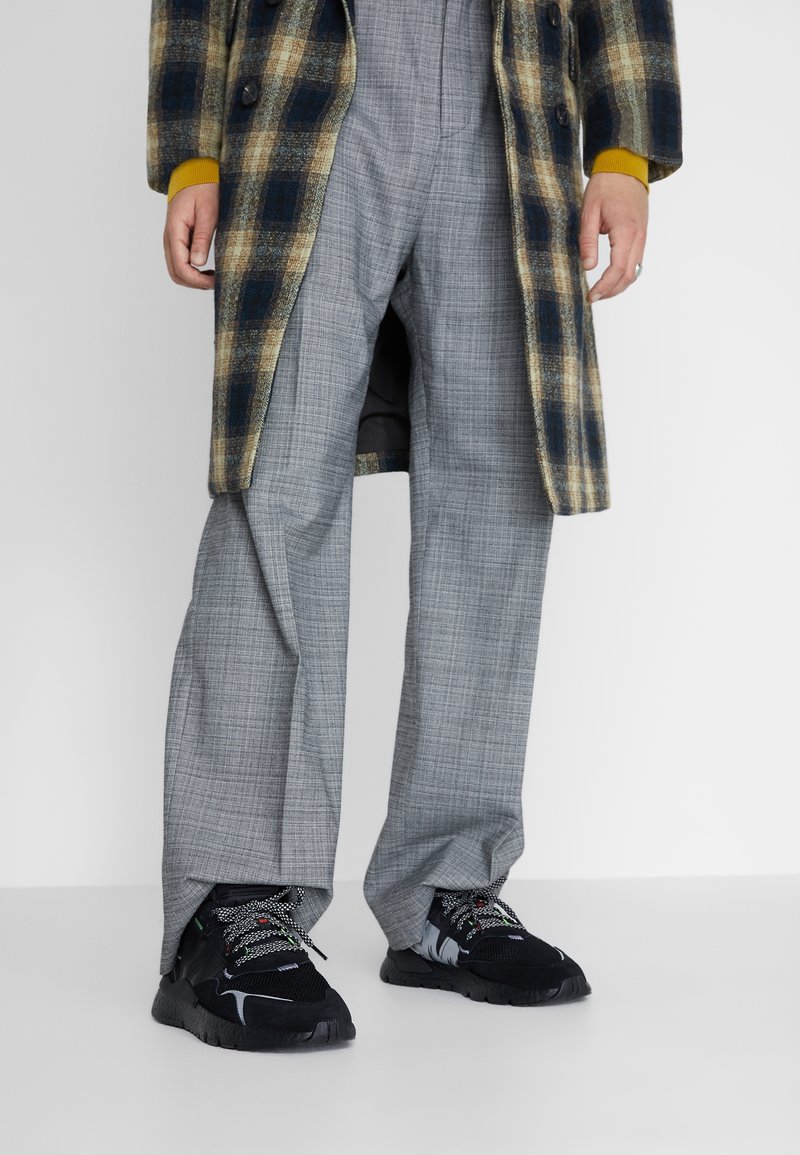 Abrigo de cuadros en marrón y azul, pantalones de cuadros grises, zapatillas negras con cordones estampados. Enfoque en las texturas y colores contrastantes.