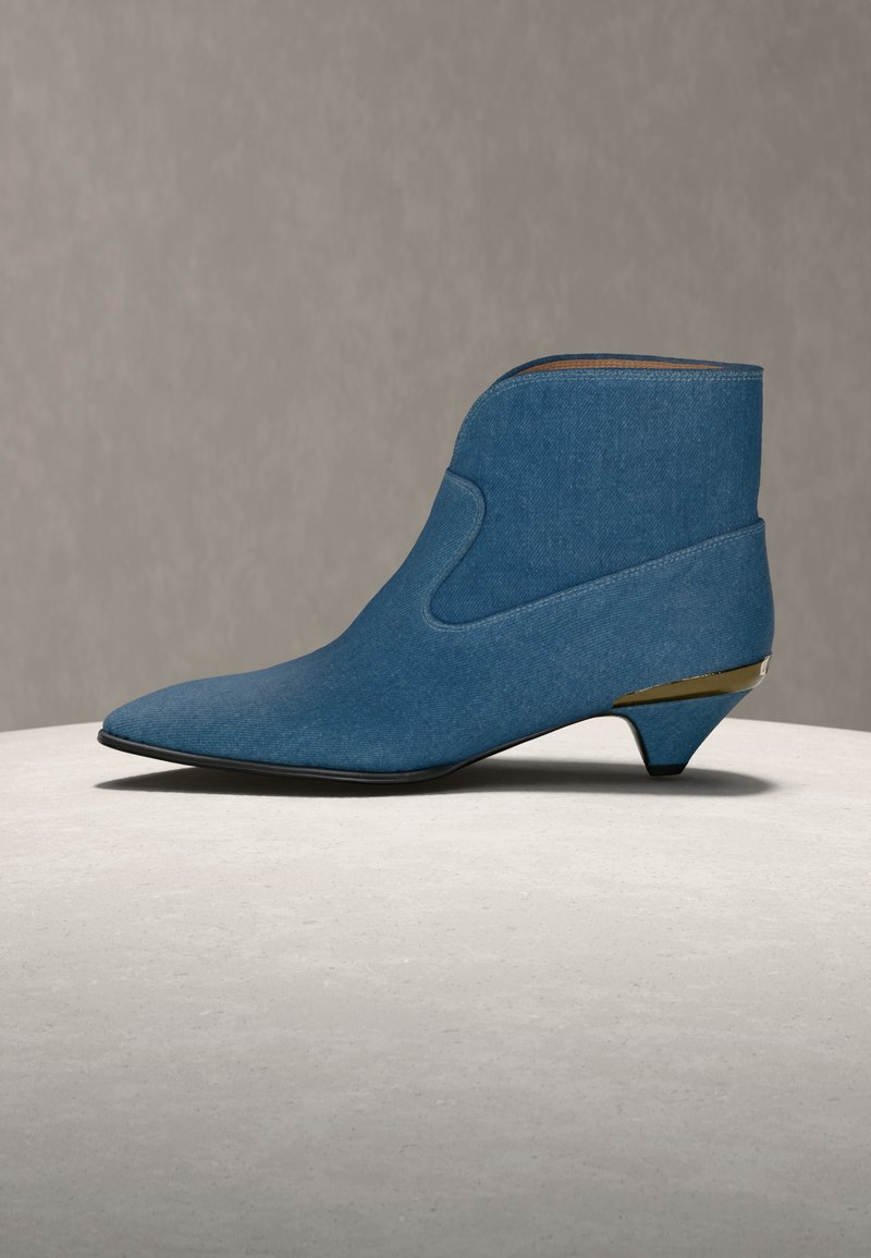 Μπλε τζιν μποτάκι αστραγάλου με μυτερή μύτη, χαμηλό τακούνι τύπου kitten και χρυσή μεταλλική λεπτομέρεια στο τακούνι, εμφανίζεται σε ανοιχτή επιφάνεια.