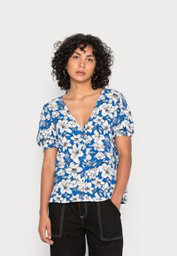 Blusa floral azul com decote em V, mangas curtas de balão, padrões de flores brancas e detalhe de botões na frente, combinada com calças pretas.