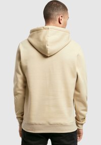 Beige hoodie med en stor, justerbar hætte, lange ærmer og ribbestrikkede manchetter. Blød stoftekstur og lige kant i taljen.