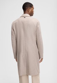 Cappotto in lana beige chiaro con colletto a pettine, una ventilazione posteriore singola e tasche laterali, caratterizzato da un design pulito e minimalista.