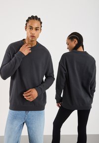 Mann som ser fremover iført svart hettegenser og lyseblå jeans, kvinne som vender bort i svart hettegenser og svarte bukser, begge med flette.