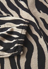 Zebraprint stof in beige en zwart met een geplooide mouwdetail, die de gladde textuur en gedurfde, contrasterende strepen toont.