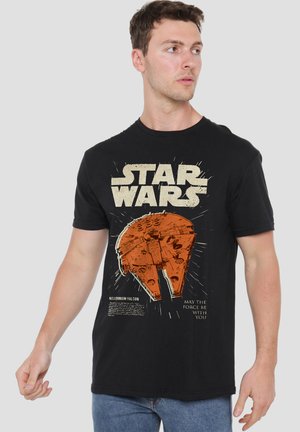 Man wearing black Star Wars t-shirt with orange Millennium Falcon graphic and text "May the Force be with you" against plain background.