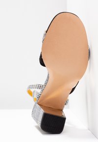 Öppen tå-häl med ett rutigt mönster i grått och svart, med ett svart rem och en slät beige sula med en strukturerad yta.