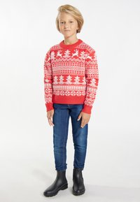 Czerwony sweter z dzianiny z białymi wzorami reniferów i śnieżynkami, okrągły dekolt, ściągacze przy mankietach, zestawiony z niebieskimi dżinsami i czarnymi botkami za kostkę.