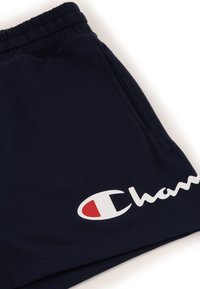 Granatowe szorty sportowe wykonane z miękkiego materiału, z elastycznym pasem i bocznymi kieszeniami. Wyraziste białe logo "Champion" z czerwonym akcentem.