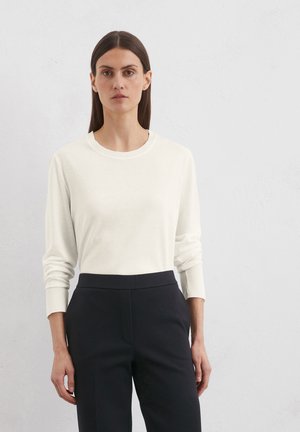 White long-sleeve shirt in soft fabric with a crew neck. Worn with black tailored pants, featuring a smooth texture and tapered fit.