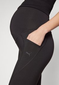 Leggings de sport noirs avec une texture lisse, dotés d'une poche latérale et d'un logo gris subtil près de la poche. Conception à taille élastique.