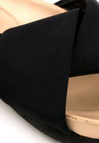 Gros plan d'une bride de sandale en tissu noir sur une semelle intérieure beige rembourrée avec une semelle noire texturée.
