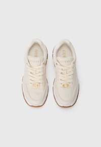 Sneaker beige con tomaia in pelle texture, suole bianche e dettagli del logo dorati. I lacci e i colli imbottiti completano il design.