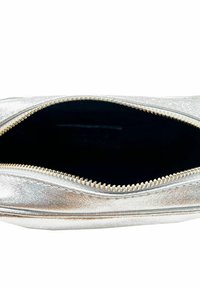 Zilveren metallic ritszak met een gladde textuur en zwarte binnenkant. Voorzien van een gouden metalen rits en stiksels langs de randen.