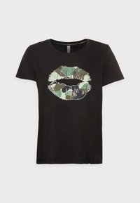 Svart kortärmad t-shirt med ett grönt och brunt kamouflagemönster av läppar i mitten. Mjuk, bomullsmaterial med rundad hals.