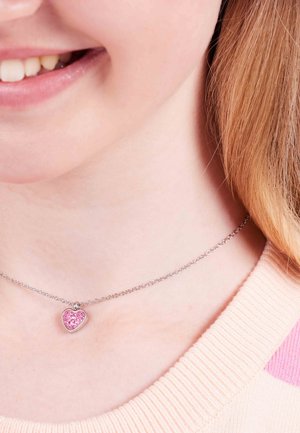 Zilveren ketting met een hartvormige hanger versierd met roze stenen, gelegen tegen een lichte trui met een ribbelkraag en roze strepen.