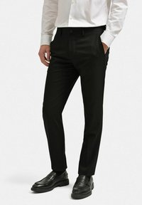 Svarta kavajbyxor i en slät väv, slim fit, med framfickor, kombinerat med svarta loafers och en vit skjorta med knappar.