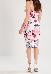 Vestido bodycon floral de tela rosa claro, con grandes flores multicolores, tirantes finos y una silueta ajustada hasta la rodilla.