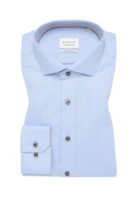 Chemise bleu clair à manches longues avec une coupe moderne. Elle présente un tissu texturé, des boutons marron et une doublure de col à motifs. Repliée soigneusement.