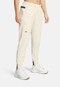 Light beige jogger pants with a textured finish, elastic waistband, side pocket with black hardware, and tapered fit. Step hem detail.