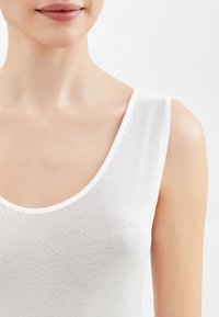 Top bianco senza maniche con scollatura a girocollo, realizzato in cotone leggero, presenta un design aderente e una superficie liscia, leggermente strutturata.