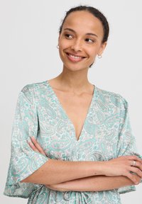 Leichtes Kleid mit Paisley-Muster in Mintgrün und Weiß, mit V-Ausschnitt, kurzen Ärmeln und einem gerafften Taillendetail.