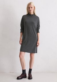 Abito grigio a maglia con maniche lunghe e colletto alto. Texture liscia. Abbinato a calze scure e mocassini marroni. Design semplice e dritto.
