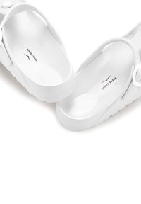 White slip-on sandals made of rubber with a textured pattern on the sole. Features a strap and logo reading "VENICE BEACH." Smooth interior.