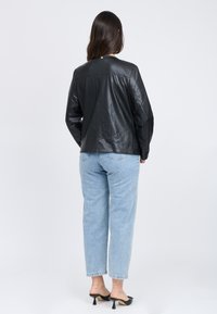 Giacca di pelle nera con una texture liscia, caratterizzata da un design semplice, abbinata a pantaloni in denim blu chiaro e scarpe nere con tacco.