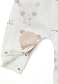 Weißer, weicher Stoffoverall mit Cartoon-Bär- und Panda-Designs in Hellbraun. Druckknopfverschluss am Knöchel für ein einfaches Anziehen.