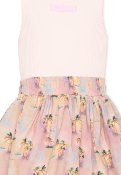 Haut blanc sans manches associé à une jupe rose pastel ornée d'un motif de palmier et d'une ceinture élastique pour un style décontracté.