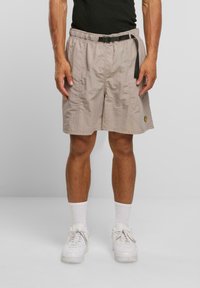 Beige Cargo-Shorts aus strukturiertem Stoff mit einem verstellbaren schwarzen Bund und einem seitlichen Logo-Patch, die knapp über dem Knie enden.
