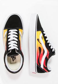 Schwarze Wildleder-Sneaker mit gelben und orangefarbenen Flammen-Designs. Sie verfügen über weiße Schnürsenkel, weiße Akzente und eine kontrastierende weiße Gummisohle.