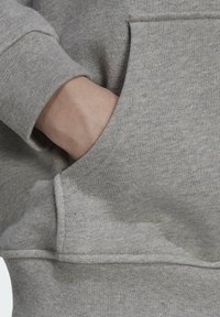 Pilkas džemperis su styga rankovėmis, turintis priekinę kengūros kišenę ir minkštą audinio tekstūrą. Matomos siuvimo detalės ant kraštų.