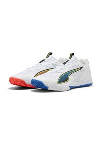 Par de zapatos deportivos blancos con detalles en los costados en negro y azul-amarillo, suela naranja en el zapato izquierdo y suela azul en el derecho, orientados hacia la derecha.