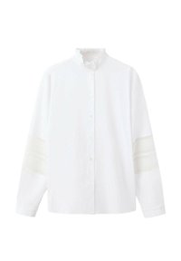 Blouse blanche à manches longues avec col volanté, boutonnage sur le devant et détails en dentelle sur le haut des manches.