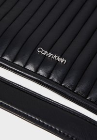 Fekete bőr táska steppelt dizájnnal, sima textúrával és fényes Calvin Klein logóval. Karcsú, téglalap alakú.