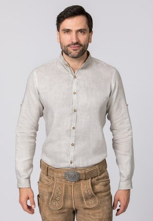 Helles graues Leinenhemd mit Stehkragen, Knöpfen vorne und umgeschlagenen Ärmeln. Getragen mit traditionellen braunen Lederhosen aus Leder, die mit floralen Stickereien verziert sind.