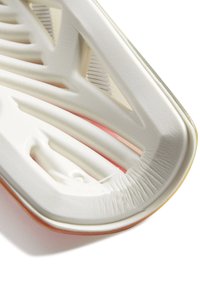 Schoenzool met een gebogen, gestructureerd profiel in wit en roze, met uitgesneden patronen en een gladde rand. Flexibel, lichtgewicht materiaal.