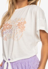 Weißes T-Shirt mit kurzen Ärmeln und floralem Design in Orange und Lavendel. Verfügt über einen geknoteten unteren Saum und eine weiche Stofftextur.