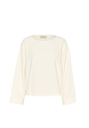 Krém színű, hosszú ujjú felső, kerek nyakkivágással, puha anyagból készült, laza szabású, felgöngyölített ujjakra jellemző. Sima felület, minimalista dizájn.