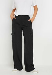 Zwarte cargo-broek met wijd rechte pijpen, voorzien van twee voorkeurszakken en twee zijzakken, met een zachte textuur en een casual pasvorm. Gecombineerd met witte sneakers.