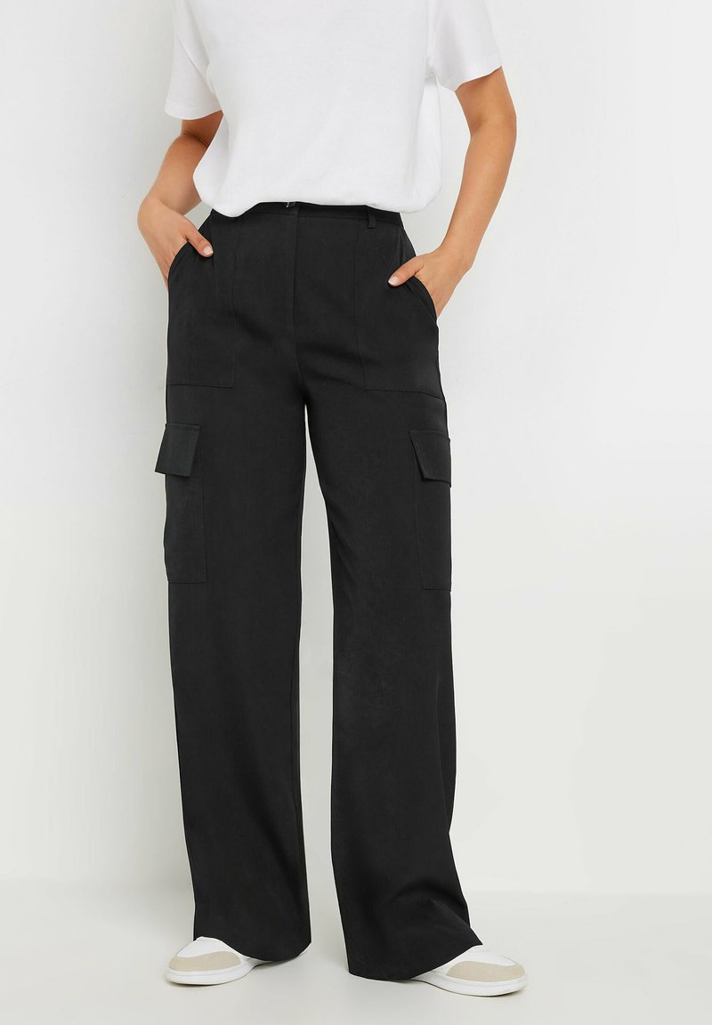Zwarte cargo-broek met wijd rechte pijpen, voorzien van twee voorkeurszakken en twee zijzakken, met een zachte textuur en een casual pasvorm. Gecombineerd met witte sneakers.